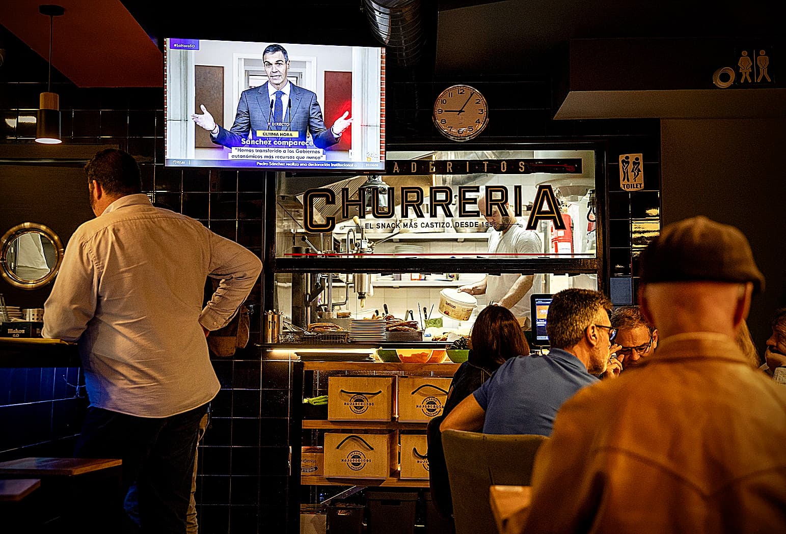 Pedro Sánchez en una conferencia con gráficos de encuestas y ambiente político tenso.