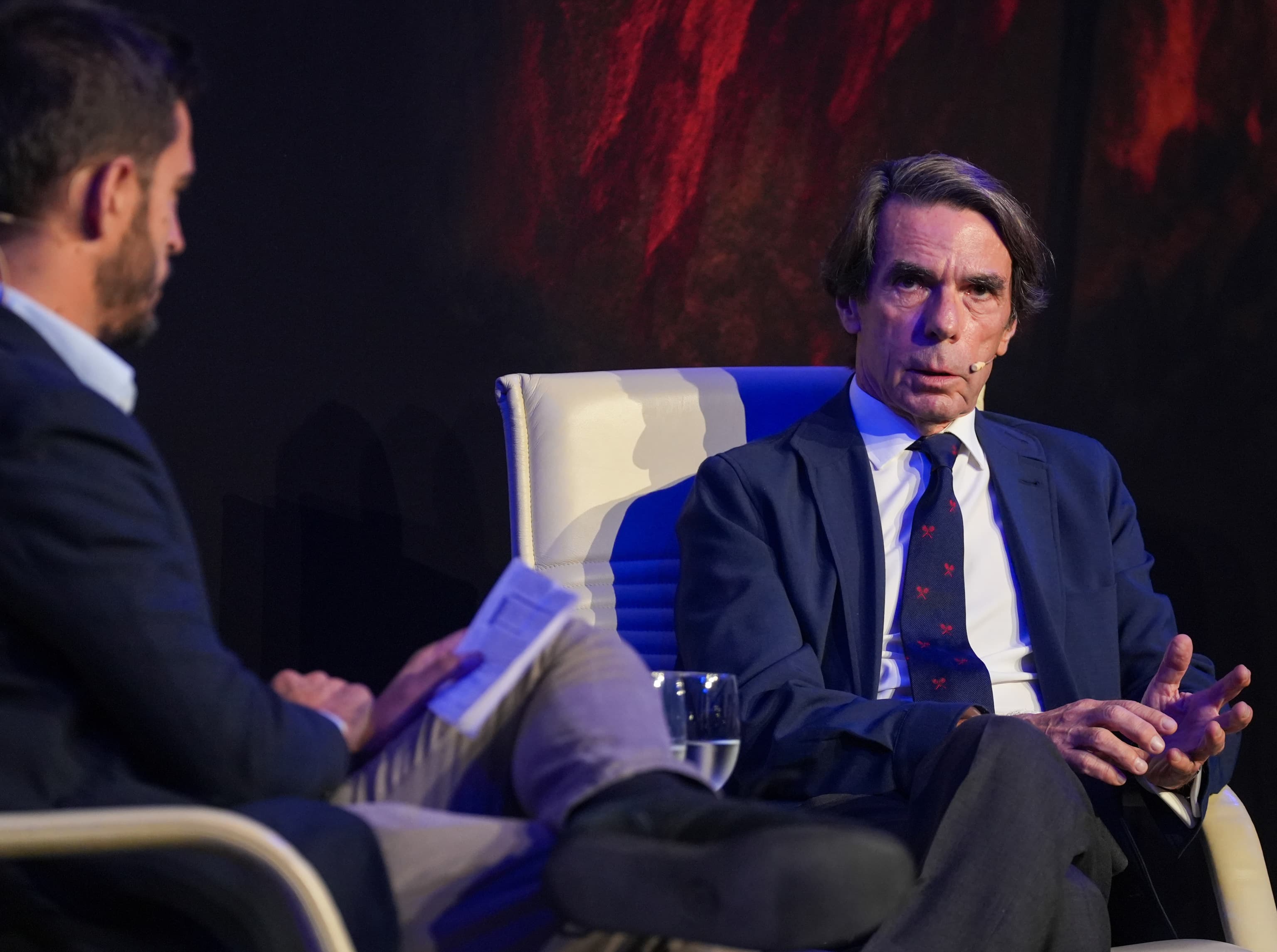 Aznar en un acto político en Andalucía, con fondo de banderas y público atento.