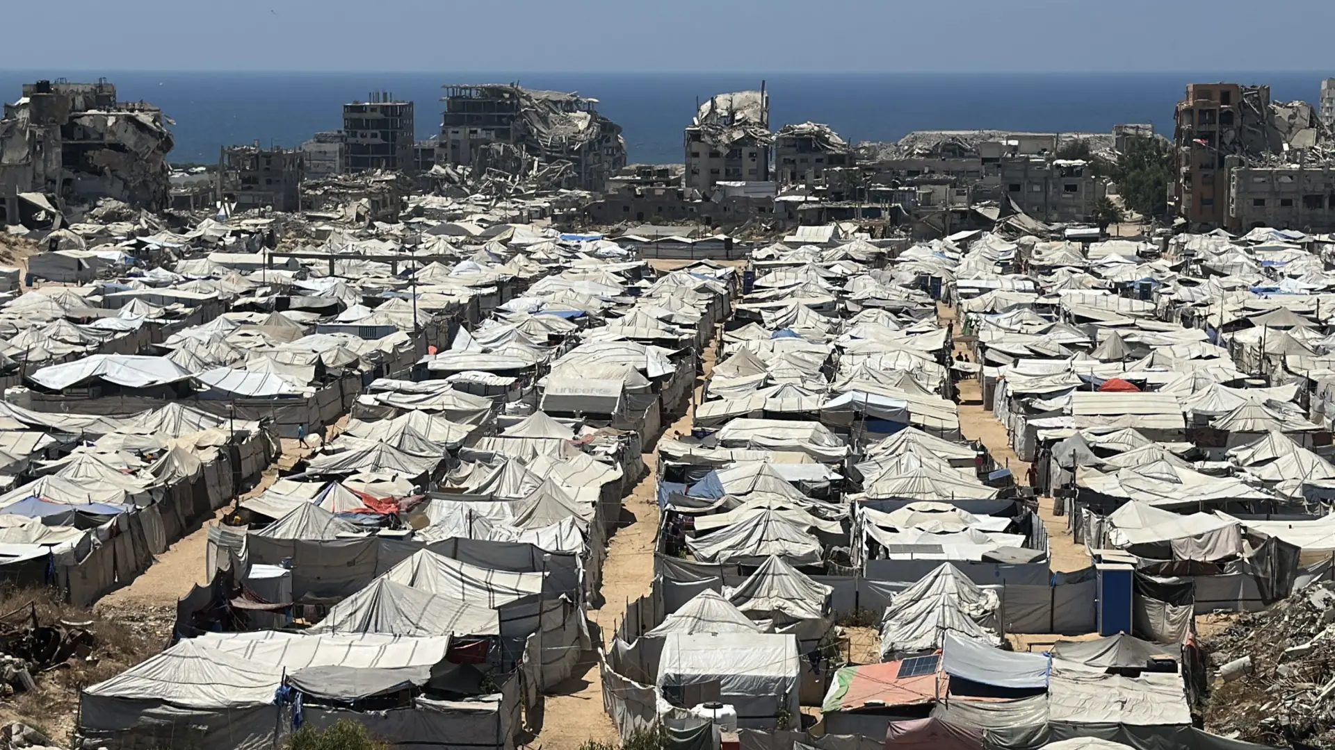 Personas en un campamento de desplazados en Gaza con infraestructura dañada